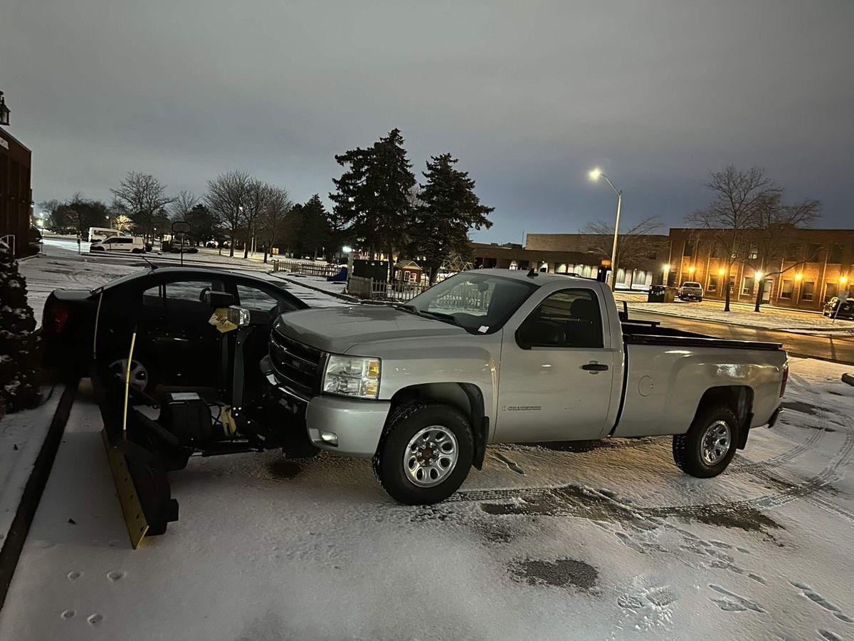 Pickup with the plow blade ready in a snowy lot at dusk