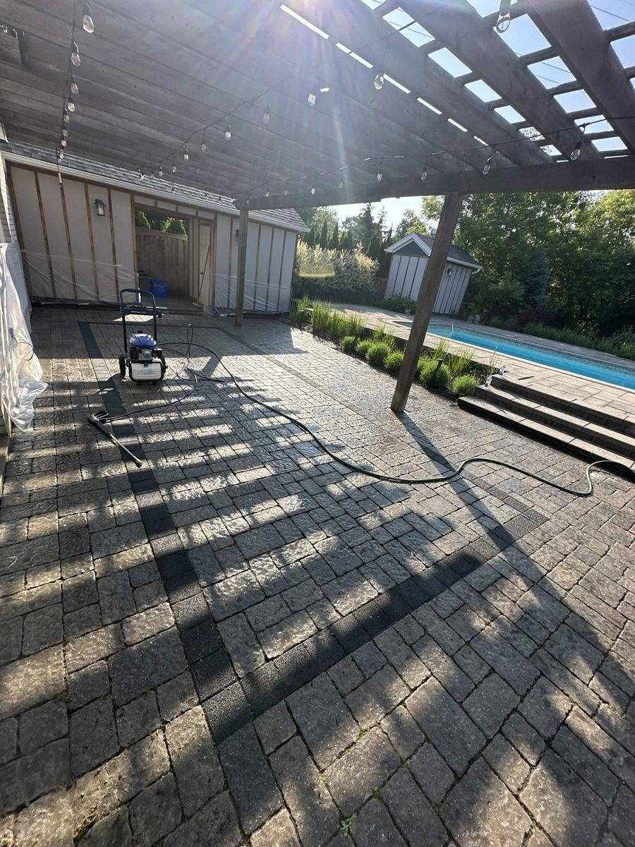 Pergola patio mid-wash, with the pressure washer and the pool beyond